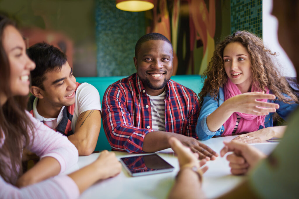 Diverse group of young adults smiling while reviewing documents together at a table.