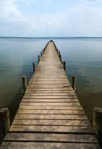 Wooden pier extending into calm lake under blue sky with distant shoreline