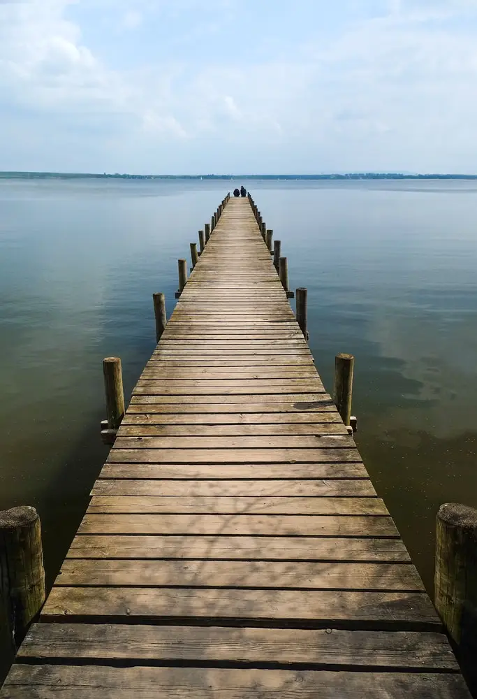 Wooden pier extending over a calm lake surrounded by trees in autumn colors.